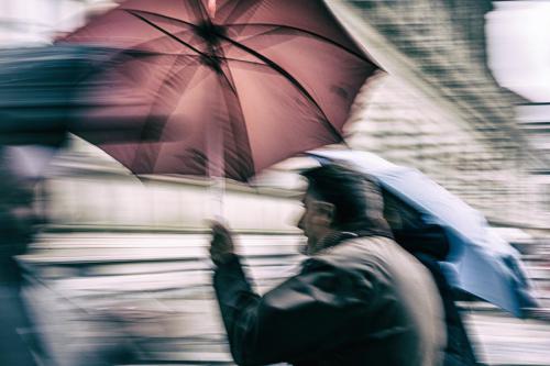 ein Mann hält einen roten Schirm gegen den Wind/Sturm 