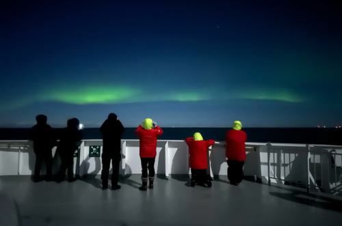 Es sind sechs Personen auf einen Schiff, die auf die Polarlichter schauen.