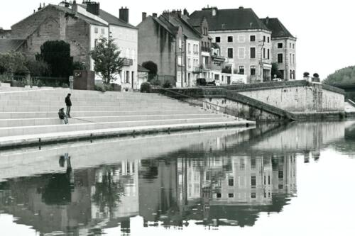 Verdun-sur-Doubs mit Passanten und Spiegelung im Wasser, schwarzweiß