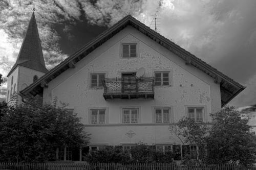 Ein alten Bauernhaus, link dahinter steht eine Kirche in schwarz weiß.